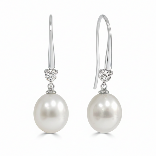 A pair of white gold drop earrings featuring a round south sea pearl and a small diamond shepards hooks.