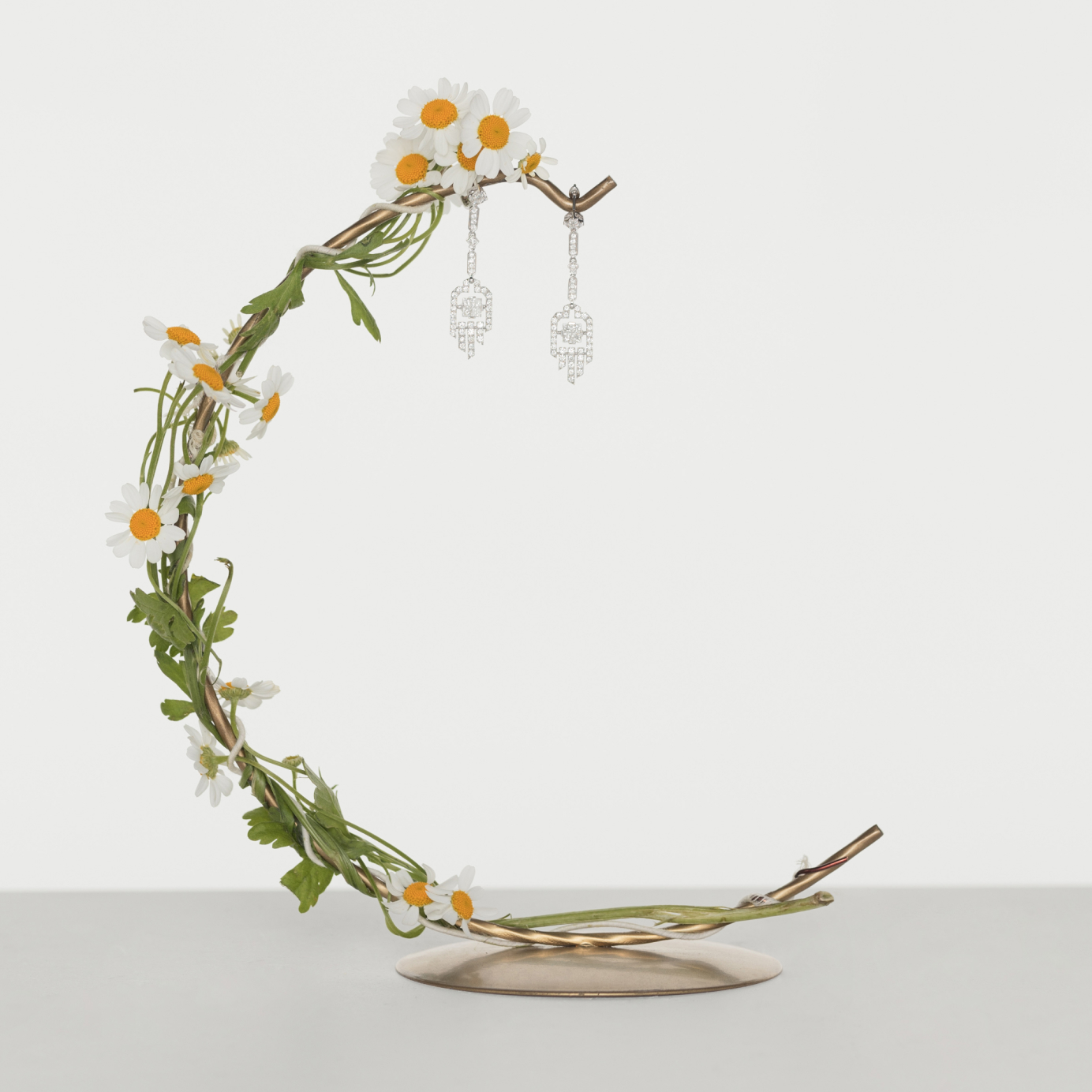 Two diamond drop earrings hang from a gold bar wrapped in daisies