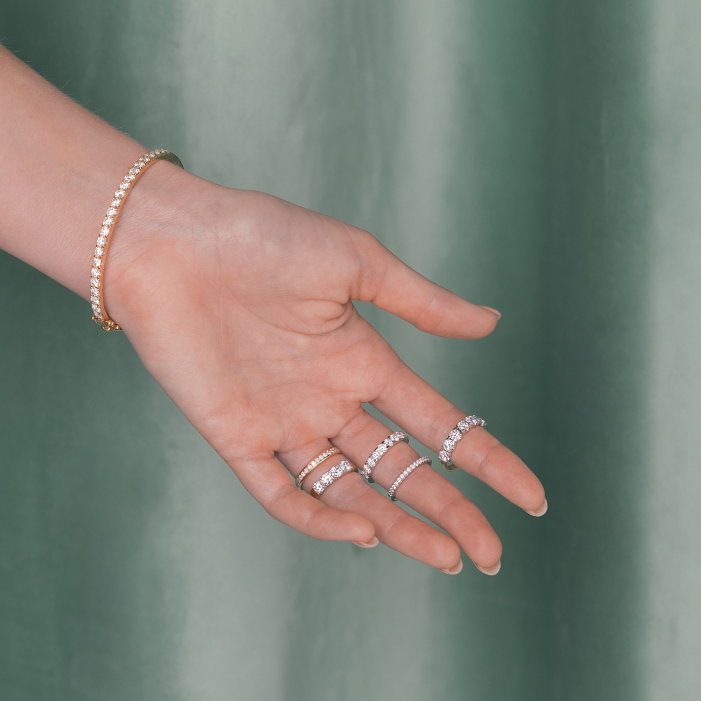 A woman's outstretched hand showcases five diamond eternity rings and a gold diamond bangle