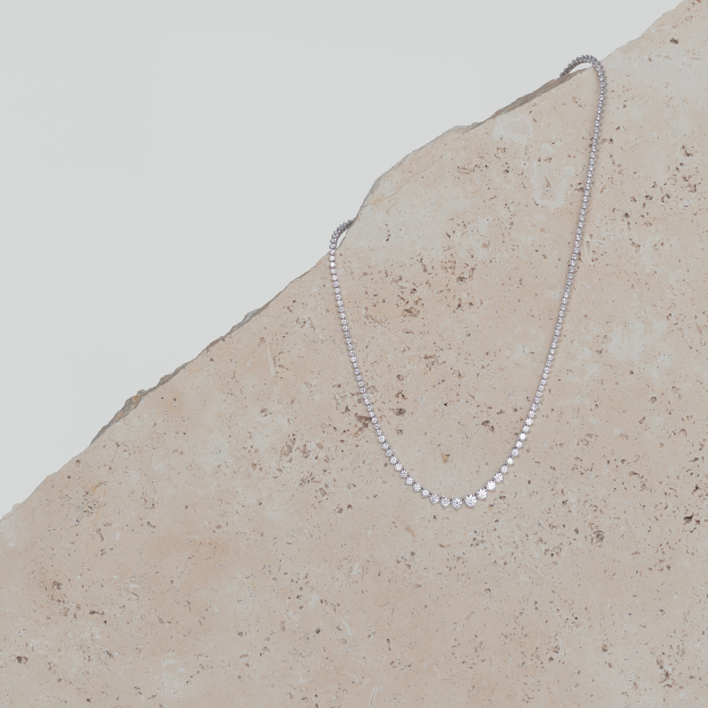 An intricate diamond necklace is draped across a stone