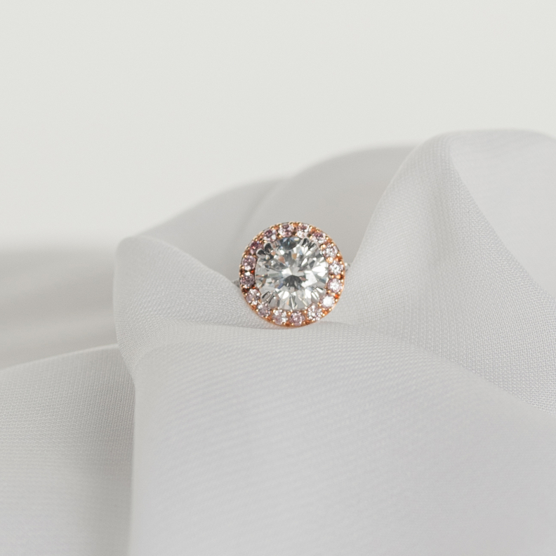 A stunning pink diamond halo surrounding a round brilliant cut diamond on a soft sheer fabric