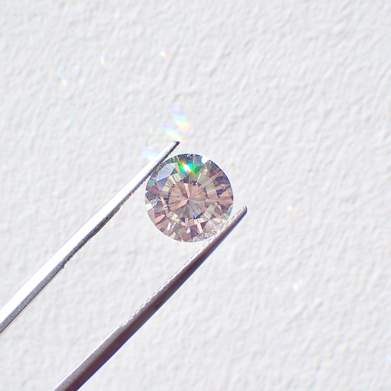 A single diamond is held up in natural light by jewellers tweezers to highlight the facet on the diamond