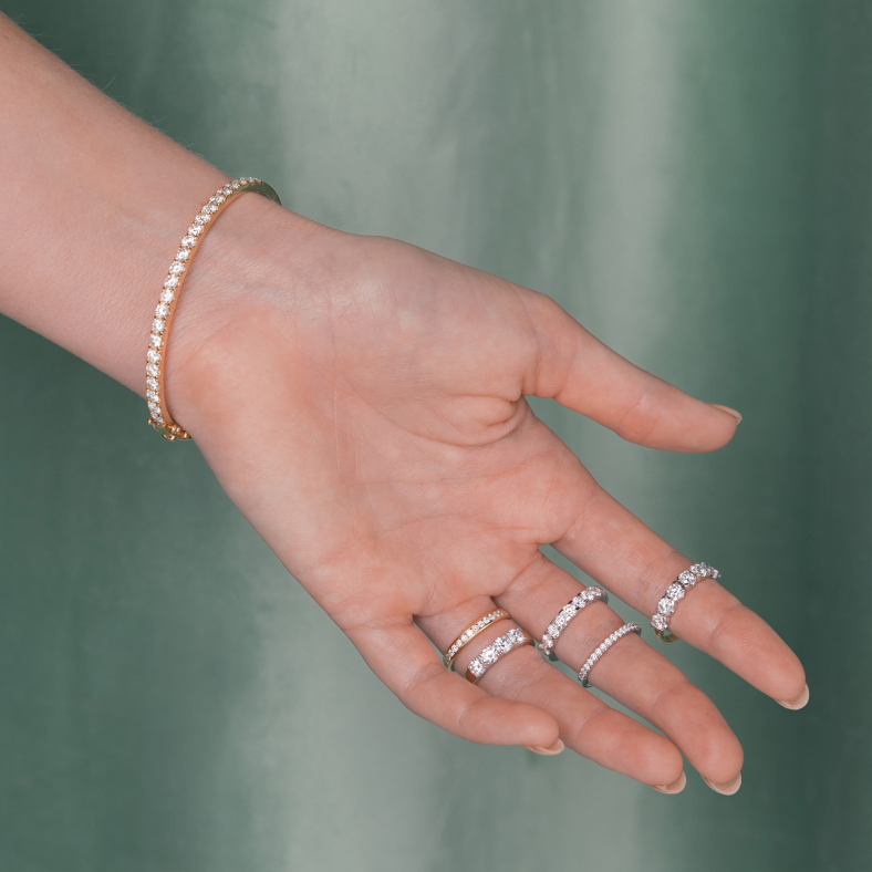 A woman's outstretched hand showcases five diamond eternity rings and a gold diamond bangle