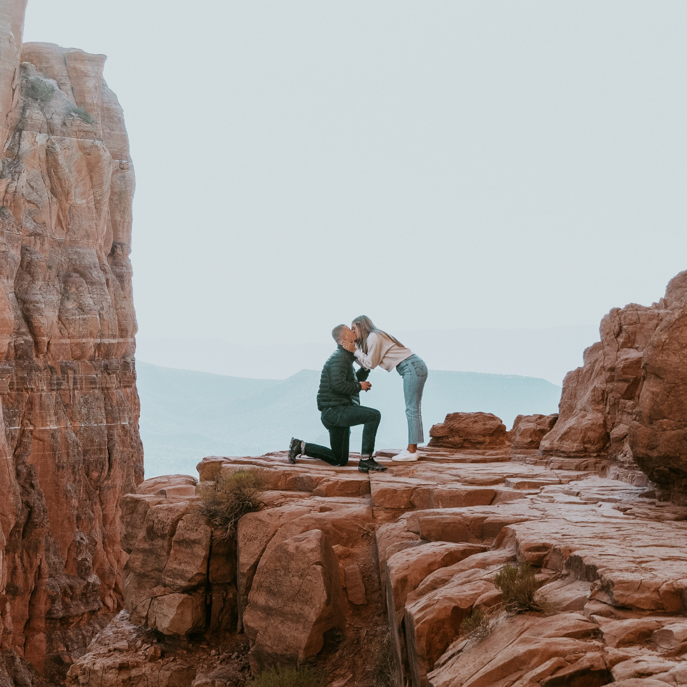 A couple kissing on a mountain after the man has proposed to his partner