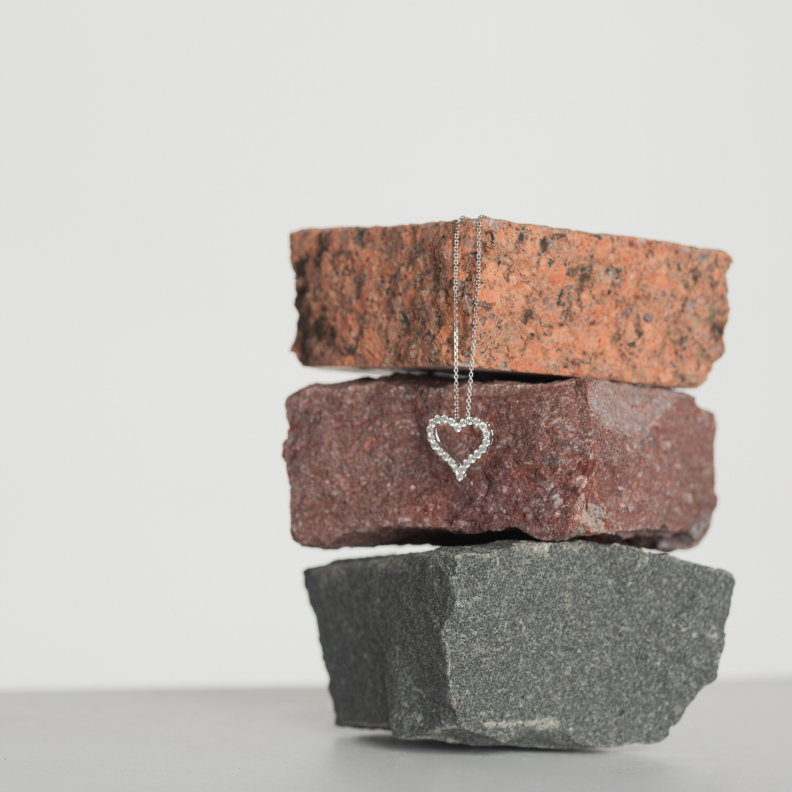 Diamond heart pendant necklace is draped across three stacked stones